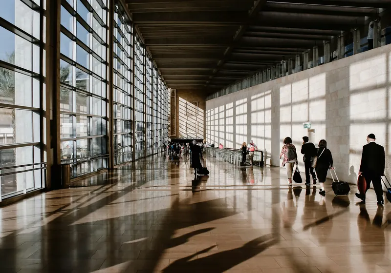 Travellers with luggage in a sunlit airport terminal